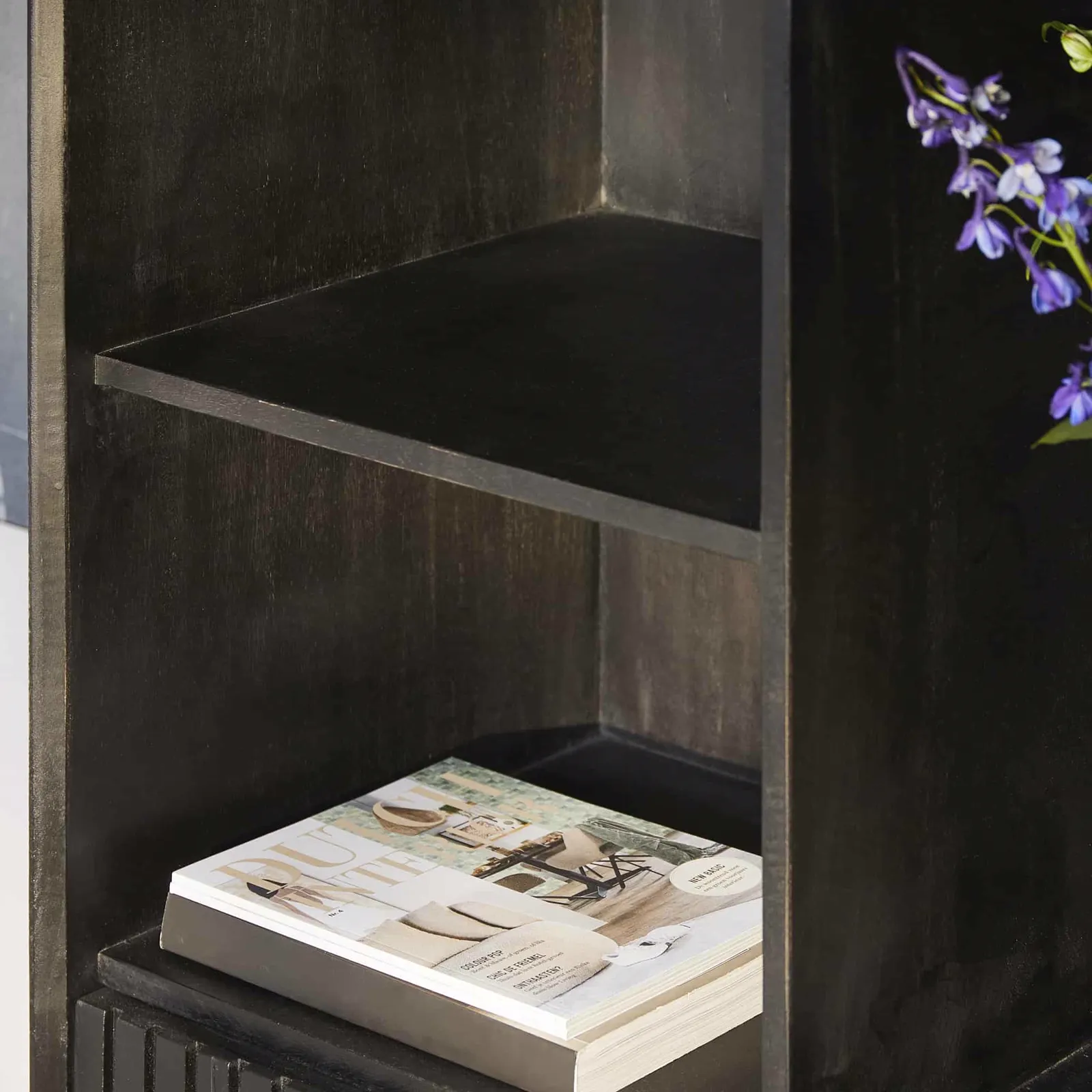 Nahaufnahme des Regalschranks Madison XL Black, mit einer Zeitschrift auf dem untersten Regal und einer Vase mit Blumen daneben - Starfurn