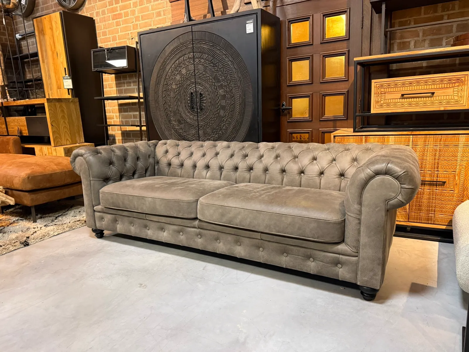 Chesterfield XL Leder 3-Sitzer Sofa in einem stimmungsvollen Showroom mit Ziegelwand und Holzmöbeln - Primavera