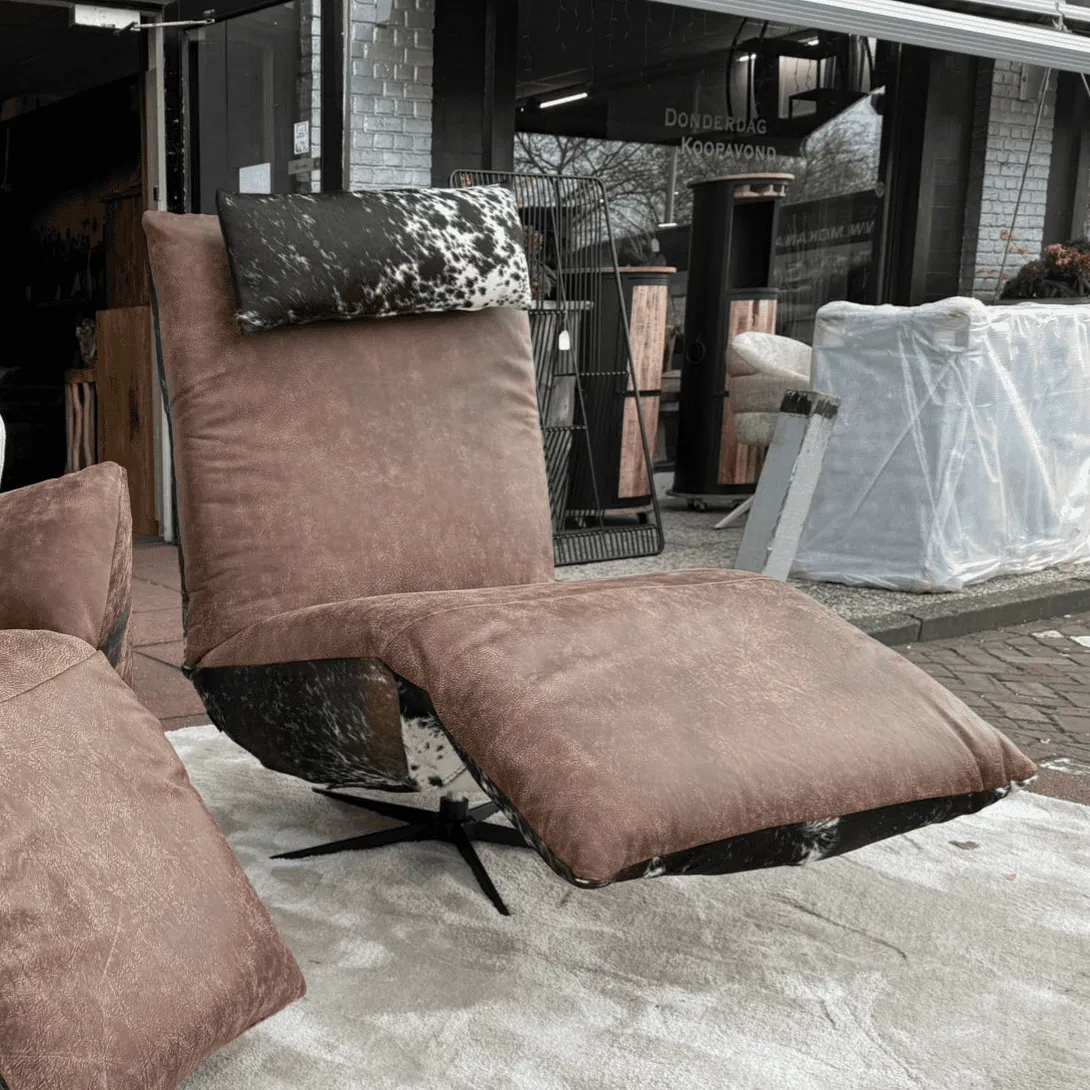 Sessel Indi mit Kuhfell und braunem Bezug, auf einem hellen Teppich vor einem Geschäft stehend - Chill-Line