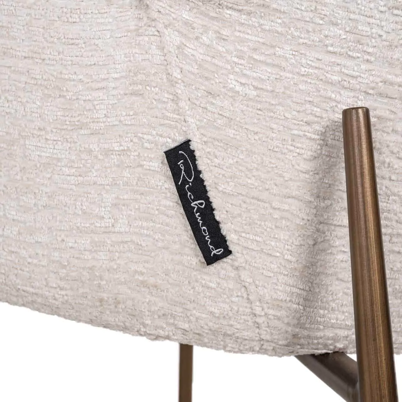 Close-up van de zitting van eetkamerstoel Amber cream fusion fire retardant, met een zwarte merklabel - Richmond Interiors