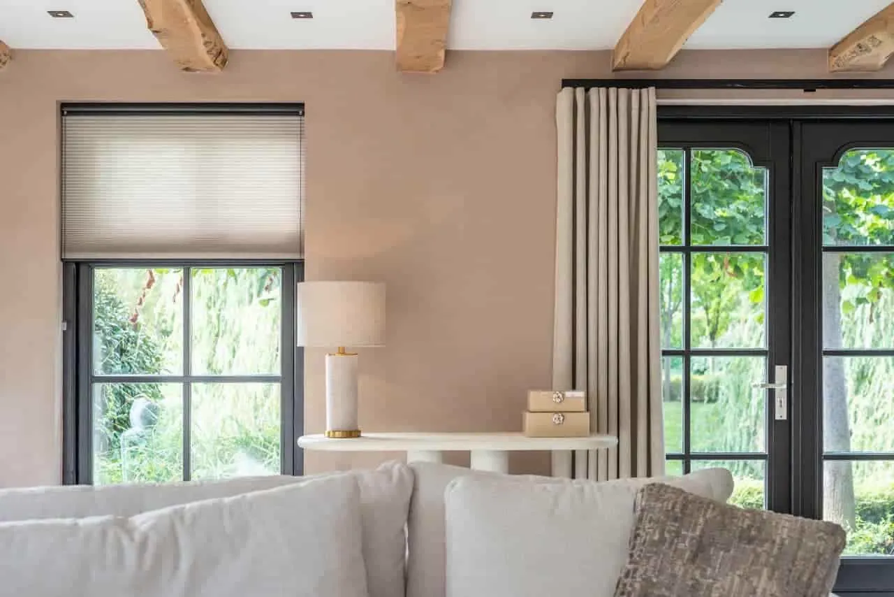 Tischleuchte Joline beige auf einem weißen Beistelltisch in einem hellen Wohnzimmer mit großen Fenstern - Richmond Interiors