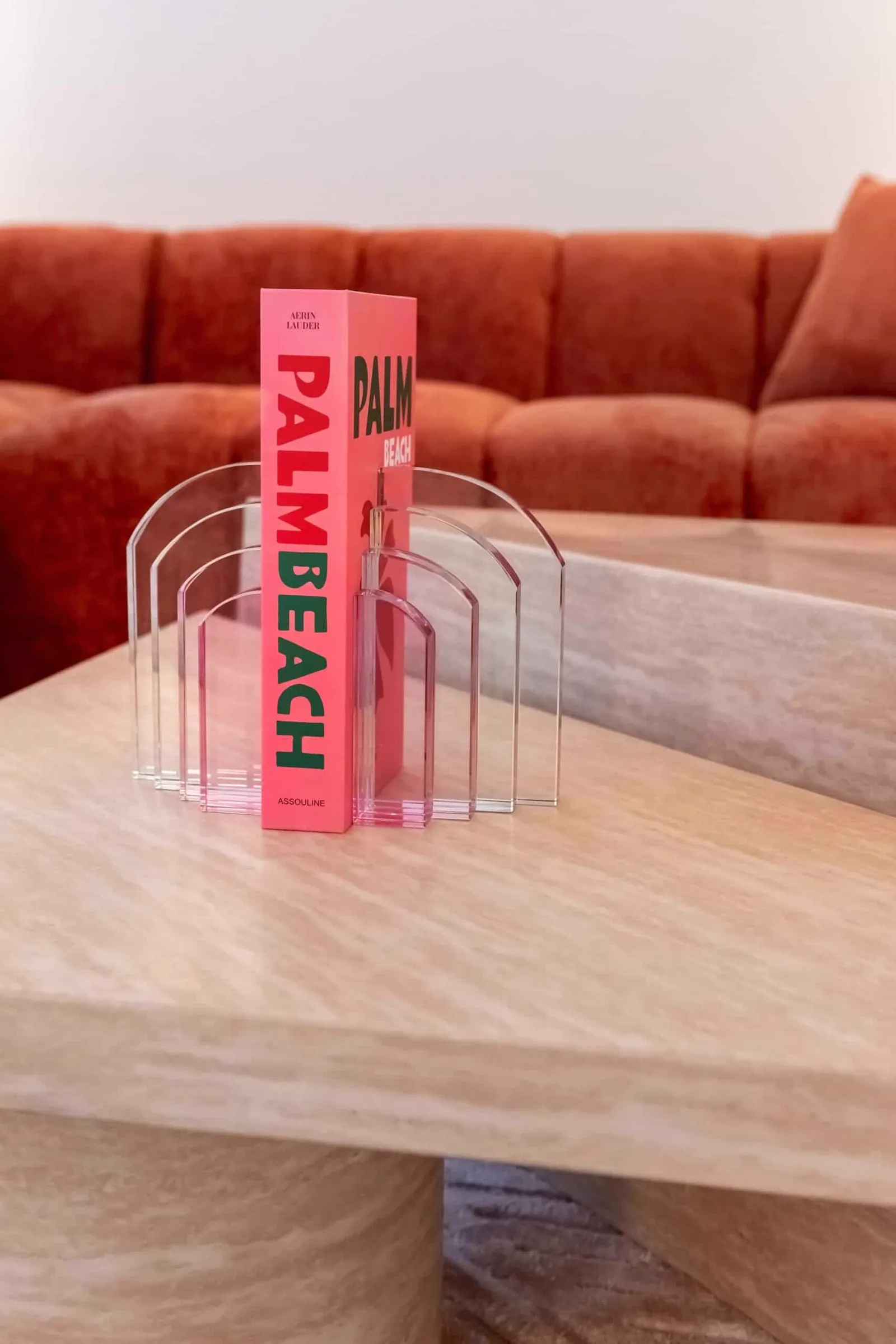 Ein pinkfarbenes Buch mit dem Titel Palm Beach steht auf einem beigen Couchtisch Fictus, mit einem orangefarbenen Sofa im Hintergrund - Richmond Interiors