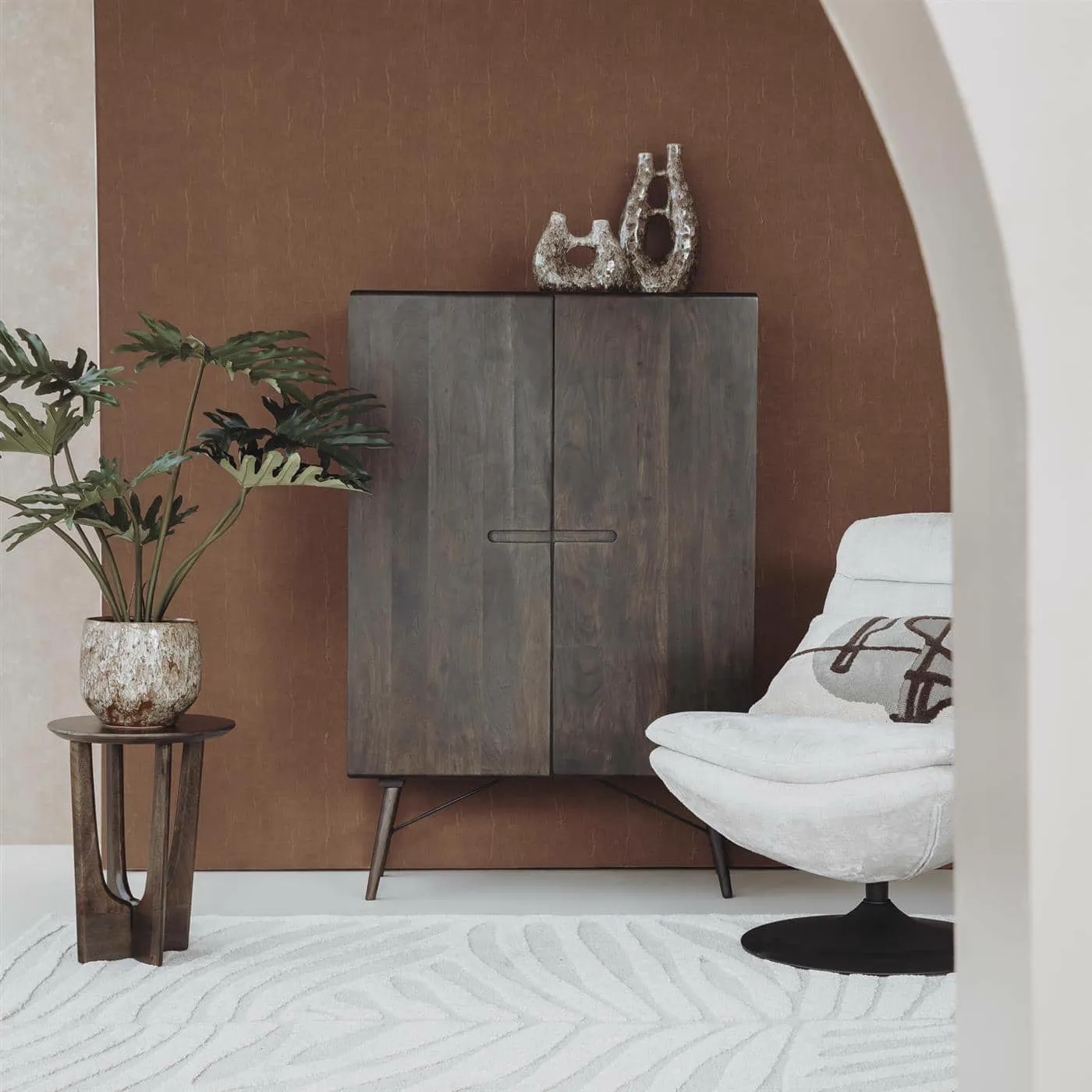 Der Aura Aufbewahrungsschrank Espresso 100 cm in einem stimmungsvollen Ambiente mit Pflanze und Sessel - Tower Living