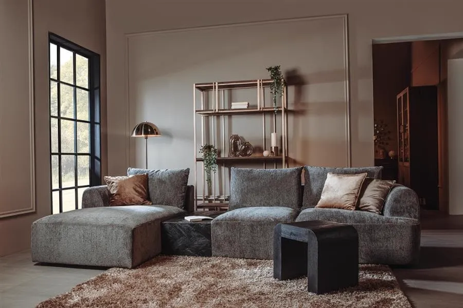 De Canterbury 2 5-AR + Chaise L - Mona 464 Cement Grey bank staat in een moderne woonkamer met een groot raam en een boekenkast - Tower Living