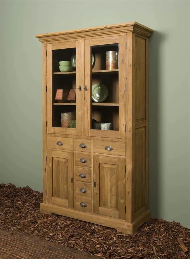 Der Bologna Vitrinenschrank 115 cm in einer Studio-Umgebung mit grüner Wand und Holzhackschnitzeln auf dem Boden - Tower Living