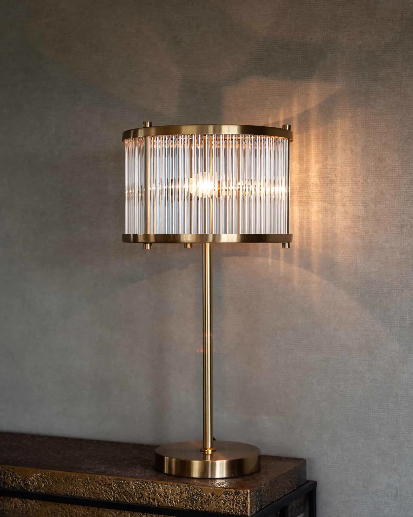 Tischleuchte Loiza Brushed Gold auf einem dunkelbraunen, strukturierten Beistelltisch vor einer grauen Wand - Richmond Interiors