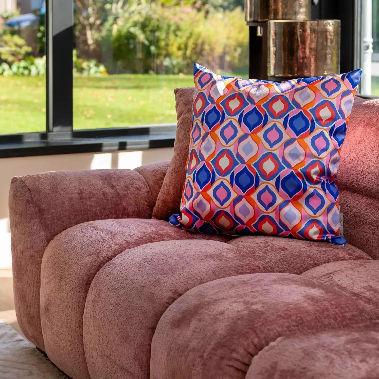 Das Sofa Charelle rose chenille steht in einem hellen Wohnzimmer mit einem Kissen und Blick auf einen Garten - Richmond Interiors