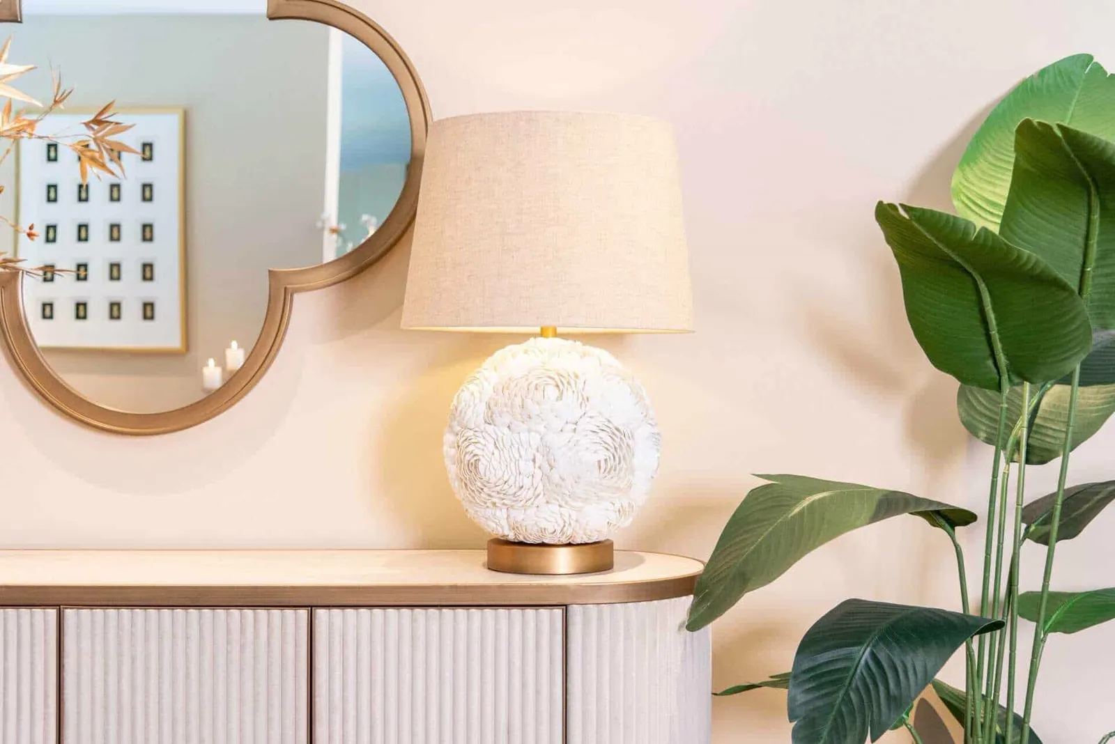 Die Tischleuchte Jamie White steht auf einem Sideboard neben einem Spiegel und einer großen grünen Pflanze - Richmond Interiors