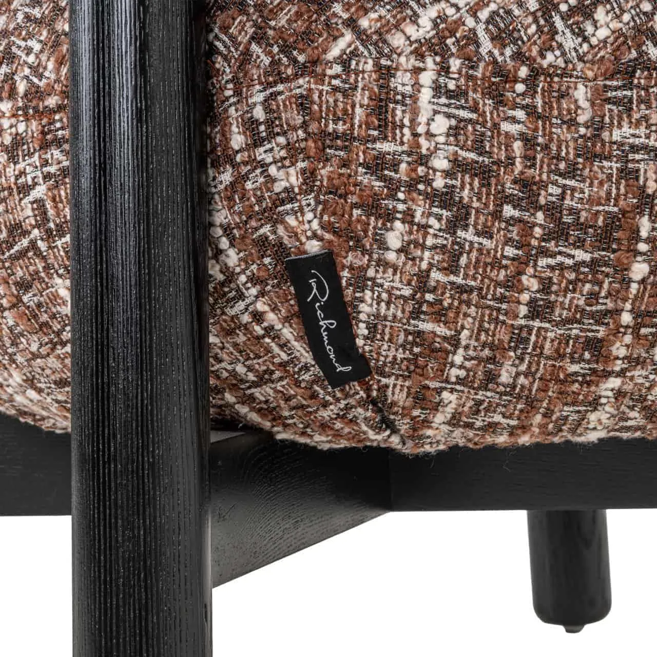 Detail des Lounge-Sessels Ornella Haselnussbraun mit Blick auf den braunen Stoff und ein schwarzes Etikett - Richmond Interiors