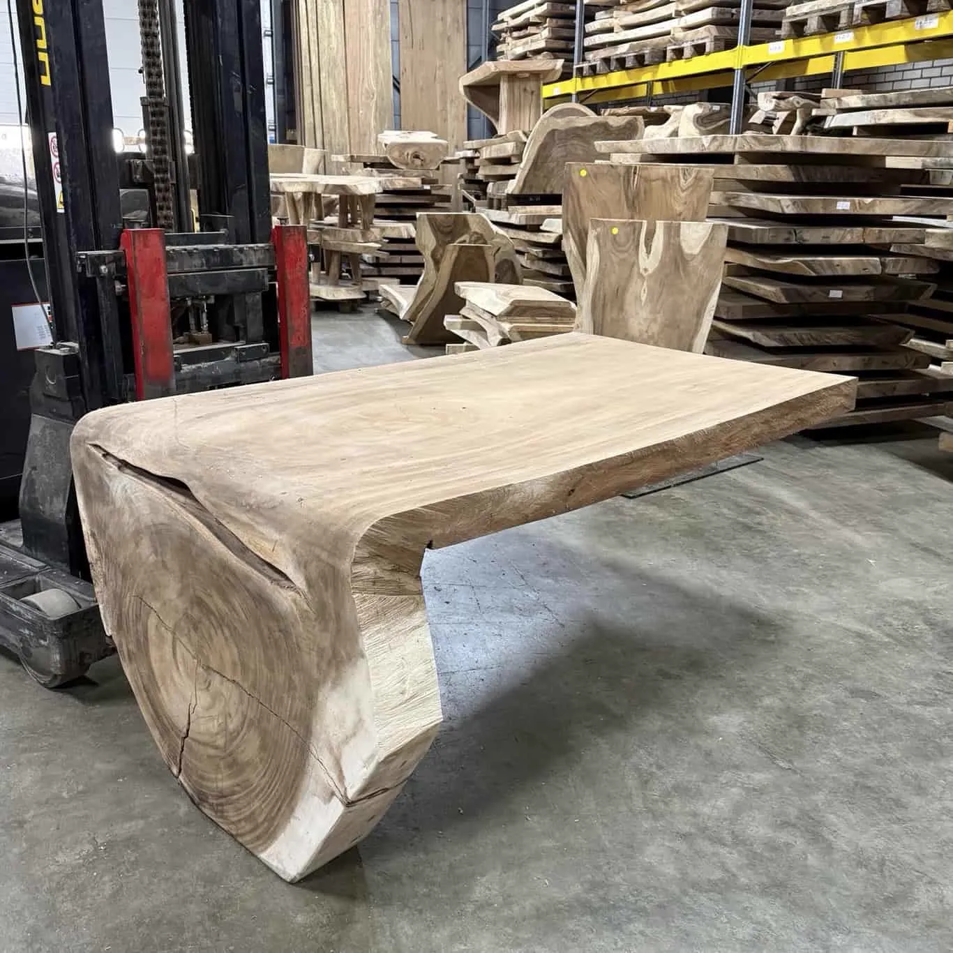 Ein Wasserfalltisch Schreibtisch 200cm aus Suarholz steht in einem Lager mit anderen Holzbrettern - World of Brosi