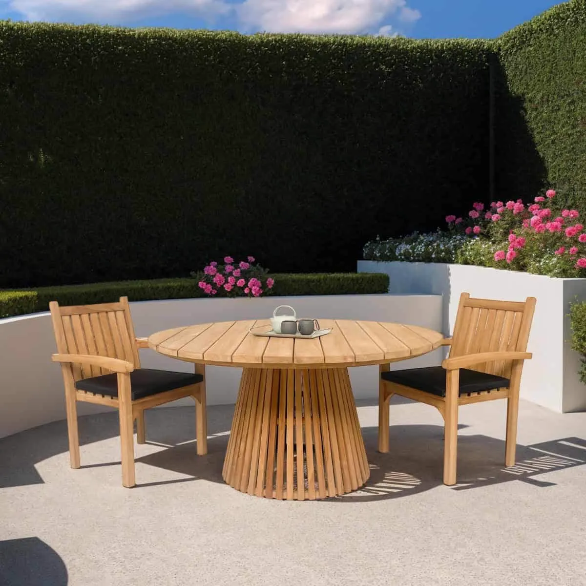 Gartenstuhl Marco Teakholz an einem runden Gartentisch in einem grünen Garten mit rosa Blumen - Livingfurn