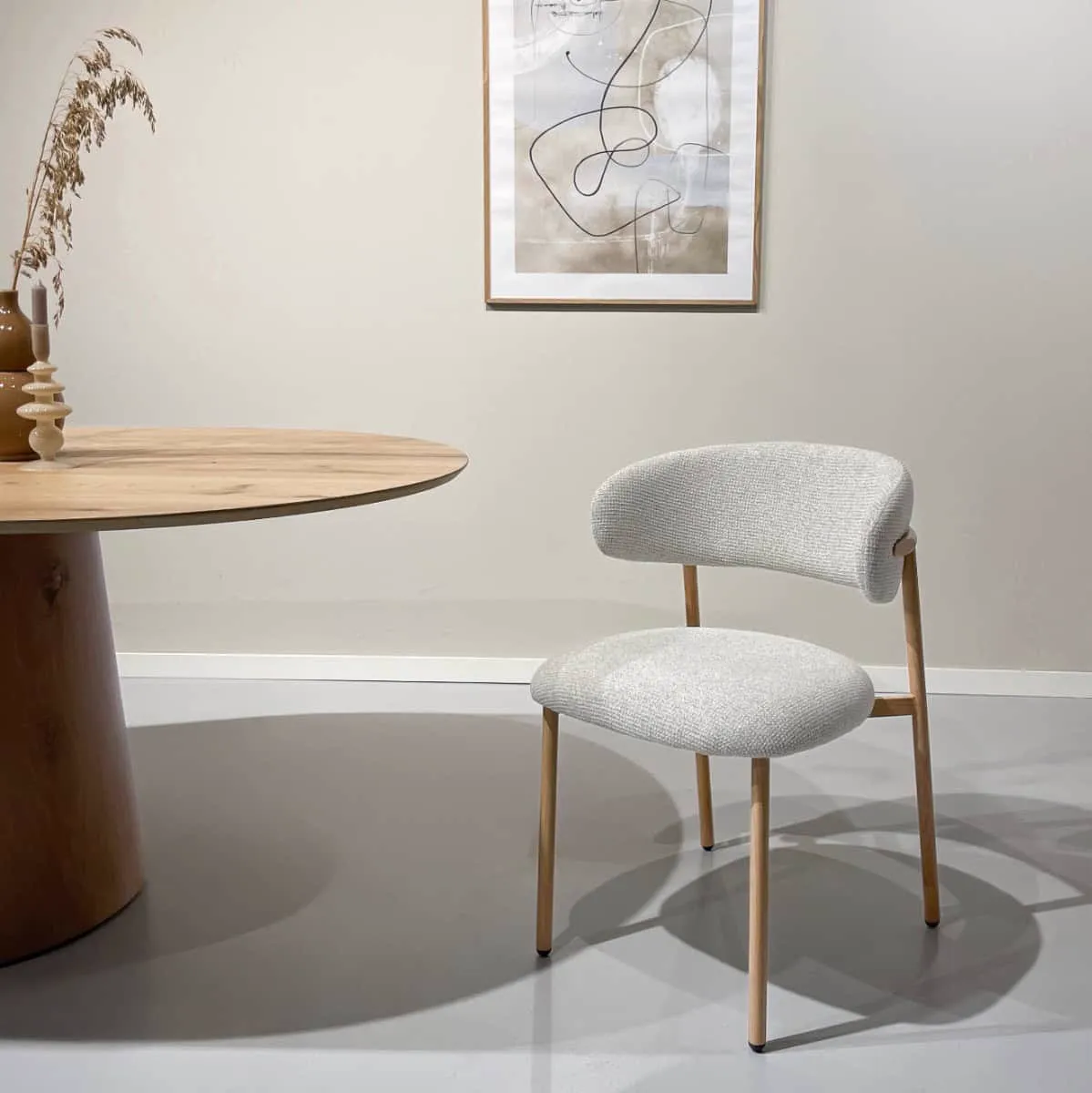 Der Micah Hush Oak Stuhl steht in einem Studio mit einem Holztisch und abstrakter Kunst an der Wand - Livingfurn