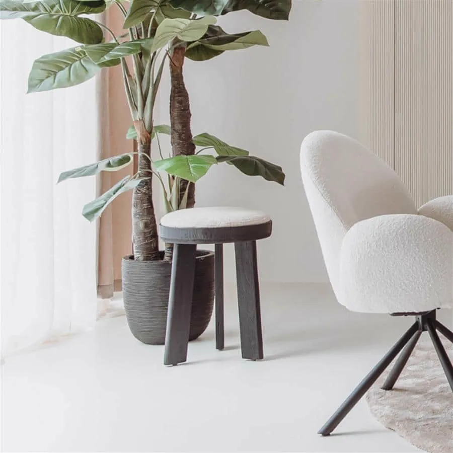 Der Ossana Hocker rund 40 cm mit heller Sitzfläche steht neben einer großen Pflanze und einem cremefarbenen Sessel - Tower Living