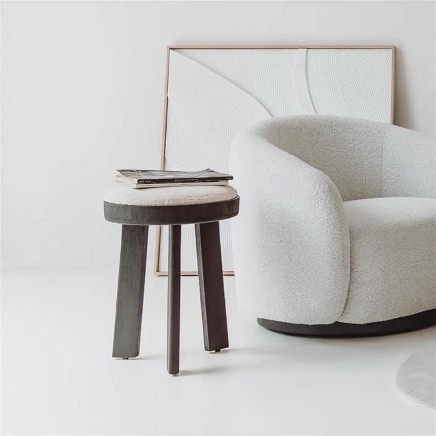 Der Ossana Hocker rund 40 cm in einem hellen Studio mit einem weißen Sessel und Kunstwerk - Tower Living