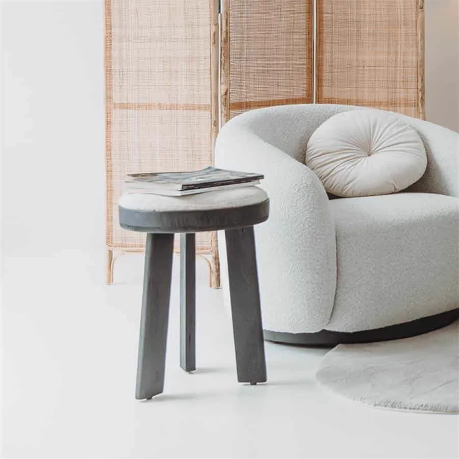 Der Ossana Hocker rund 40 cm mit Zeitschriften in einem hellen Wohnzimmer neben einem Sessel - Tower Living