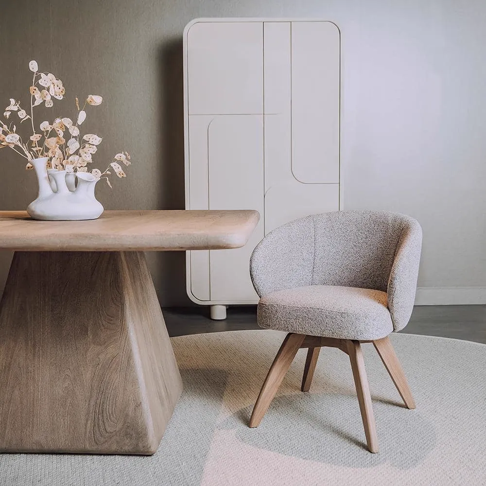 Der drehbare Brescia Sessel aus hellgrauem Stoff steht auf einem runden Teppich neben einem Holztisch - Tower Living