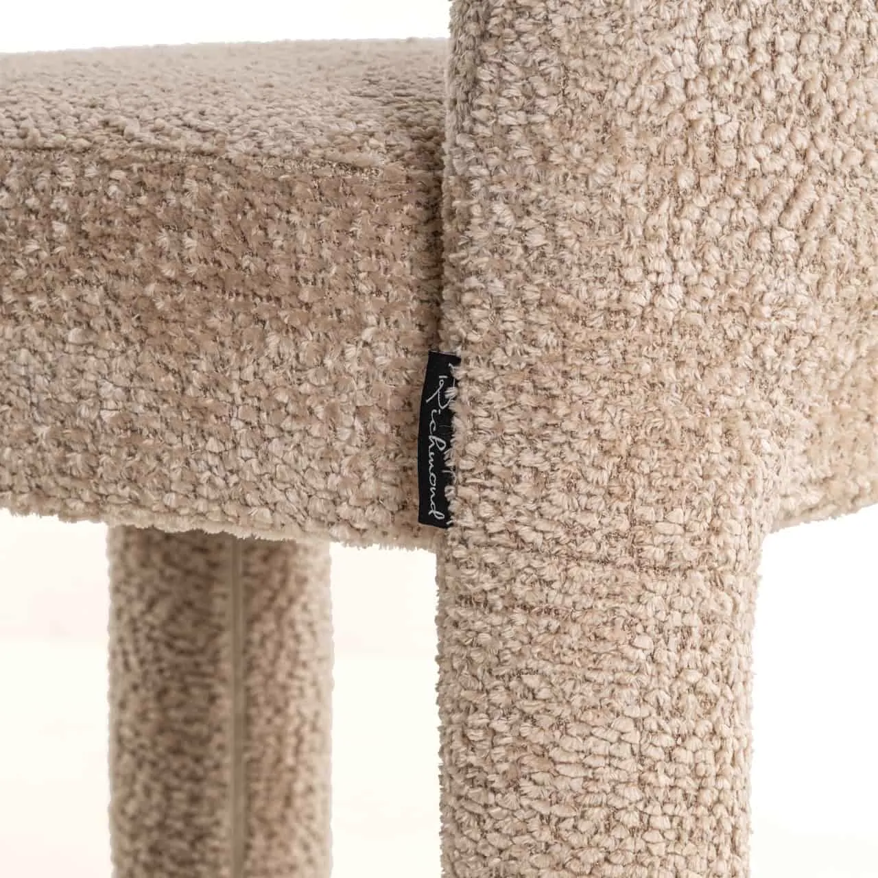 Nahaufnahme der Sitzfläche und des Beins des Esstuhls Brandi lovely beige, mit Blick auf die Textur und das Markenetikett - Richmond Interiors