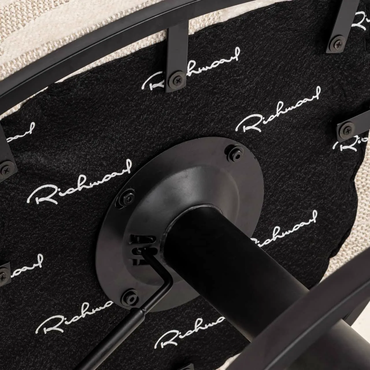 Detailaufnahme der Unterseite des Barhocker Cheyenne beige graffic swivel, mit dem schwarzen Metall-Drehmechanismus und dem Markennamen 'Richmond' auf dem Stoff - Richmond Interiors