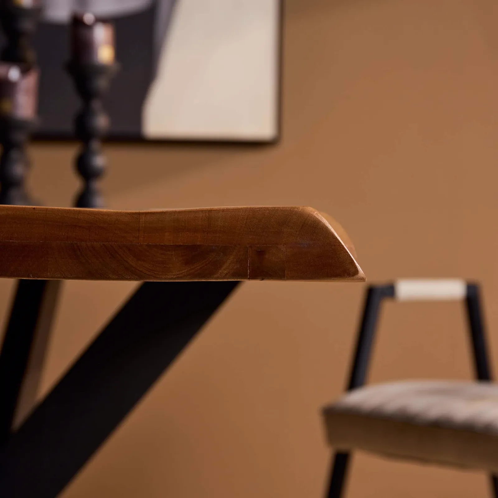 Detail des Baumstammtisch Boston Natur Mangoholz 220 cm, mit der Kante der Tischplatte und einem Stuhl im Hintergrund - Starfurn