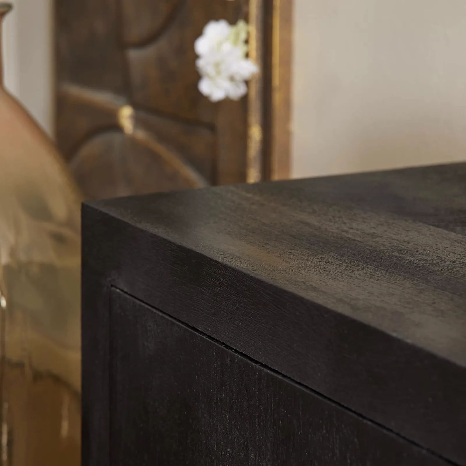 Detailaufnahme der dunklen Holzmaserung und klaren Linien des TV-Möbels Brüssel Black, mit einer Vase und Dekoration im Hintergrund - Starfurn