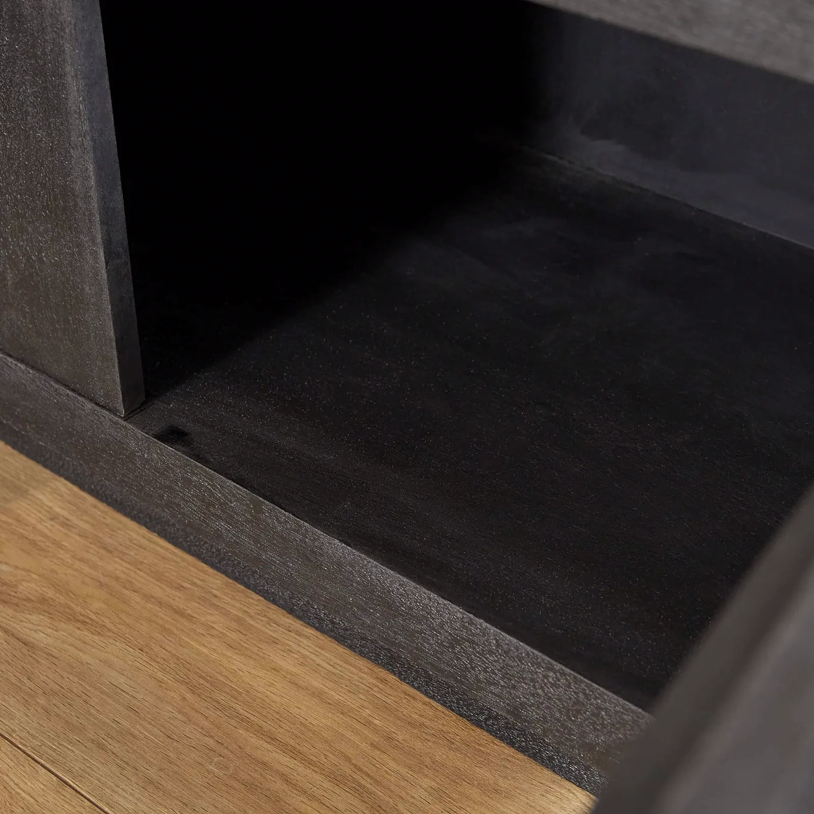 Nahaufnahme der Innenseite des schwarzen TV-Schrank Brüssel Black, mit einem Holzboden im Vordergrund - Starfurn
