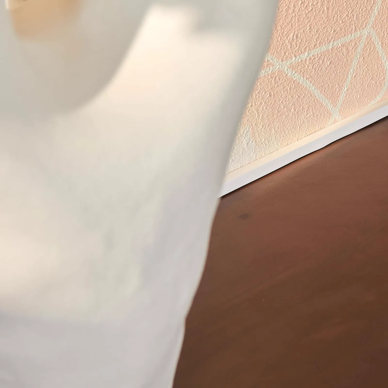Detailaufnahme des Couchtischs Brussel Walnut, mit einer glänzenden braunen Oberfläche und einer hellen Sockelleiste an einer rosa Wand - Starfurn