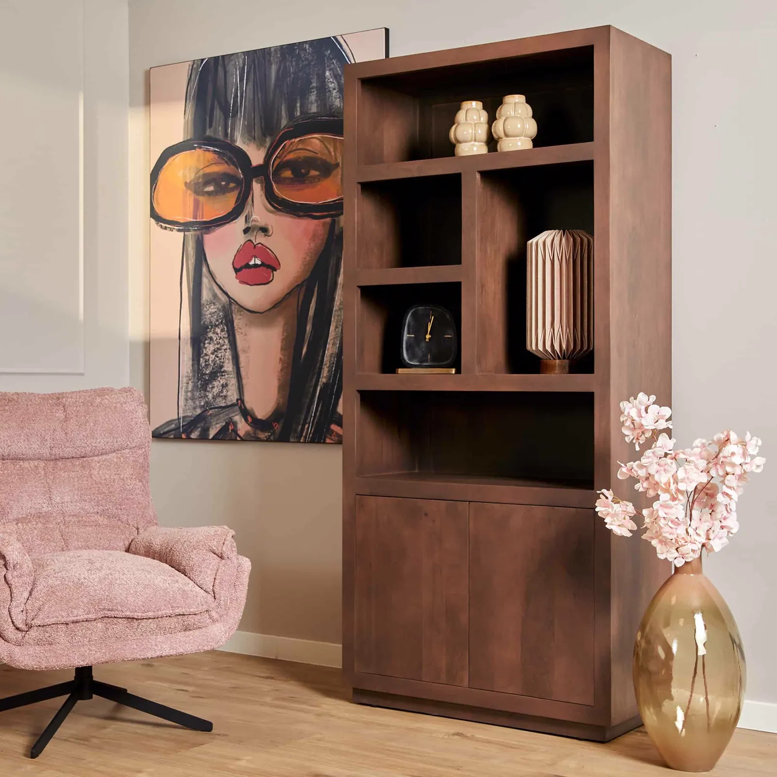 Ein rosa Sessel steht neben einem braunen Bücherregal mit Dekoration, im Hintergrund ein Kunstwerk einer Frau mit Sonnenbrille - Starfurn