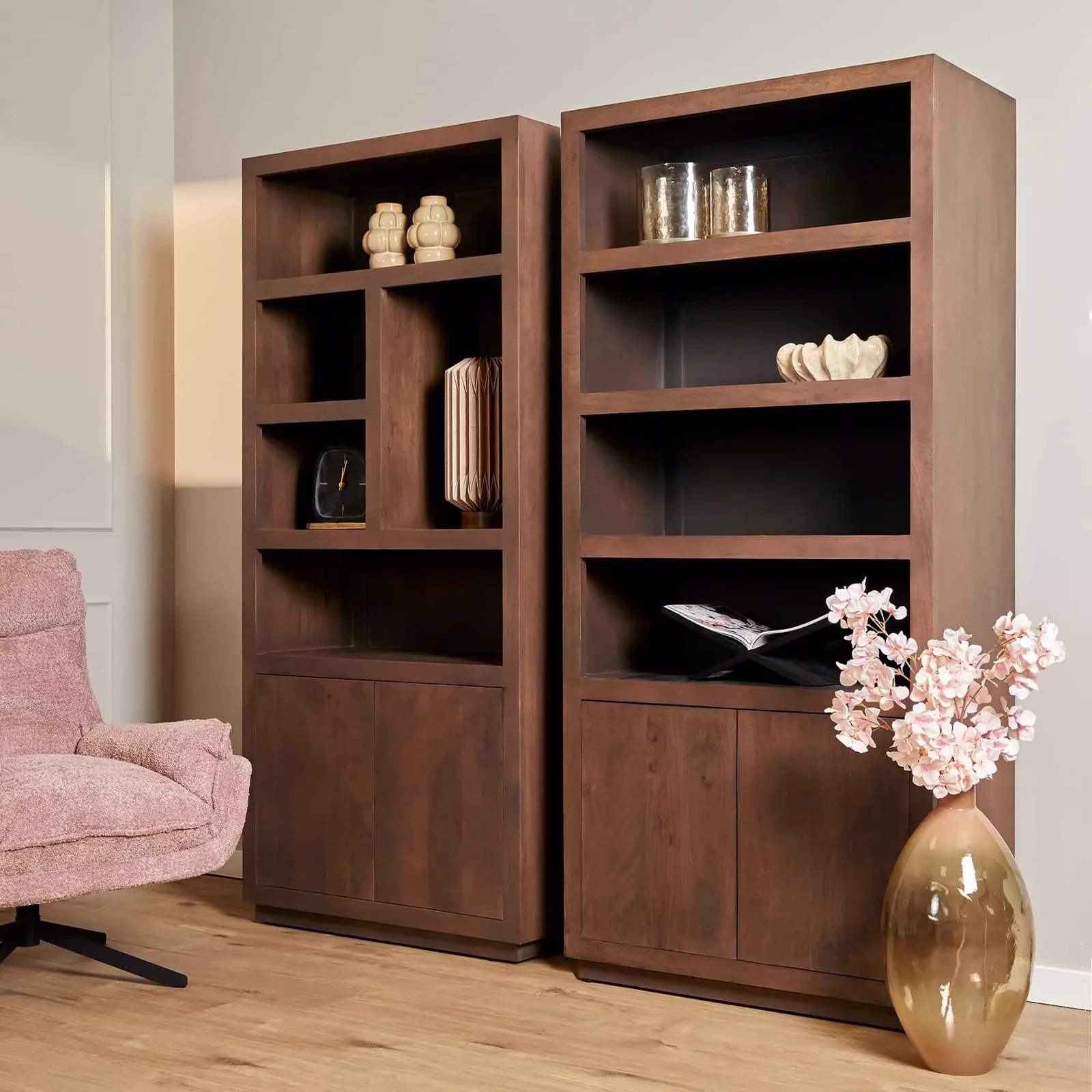 Twee donkerhouten boekenkasten met open schappen en dichte kasten, staand naast een roze fauteuil in een lichte woonkamer - Starfurn