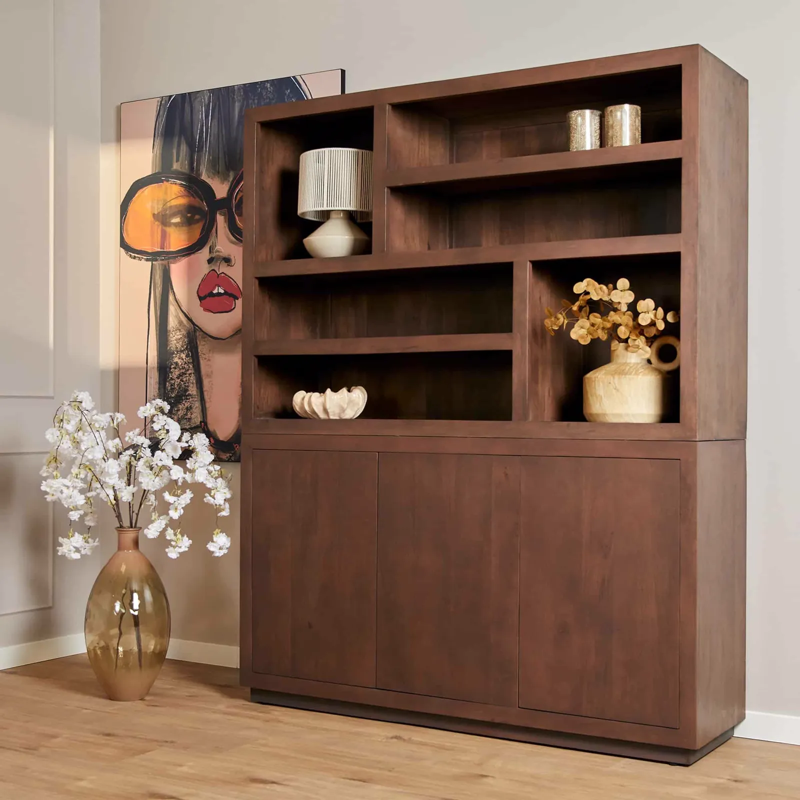 Een donkerbruine boekenkast met open vakken en dichte kasten, staand in een woonkamer met een kunstwerk en een vaas met bloemen ernaast - Starfurn