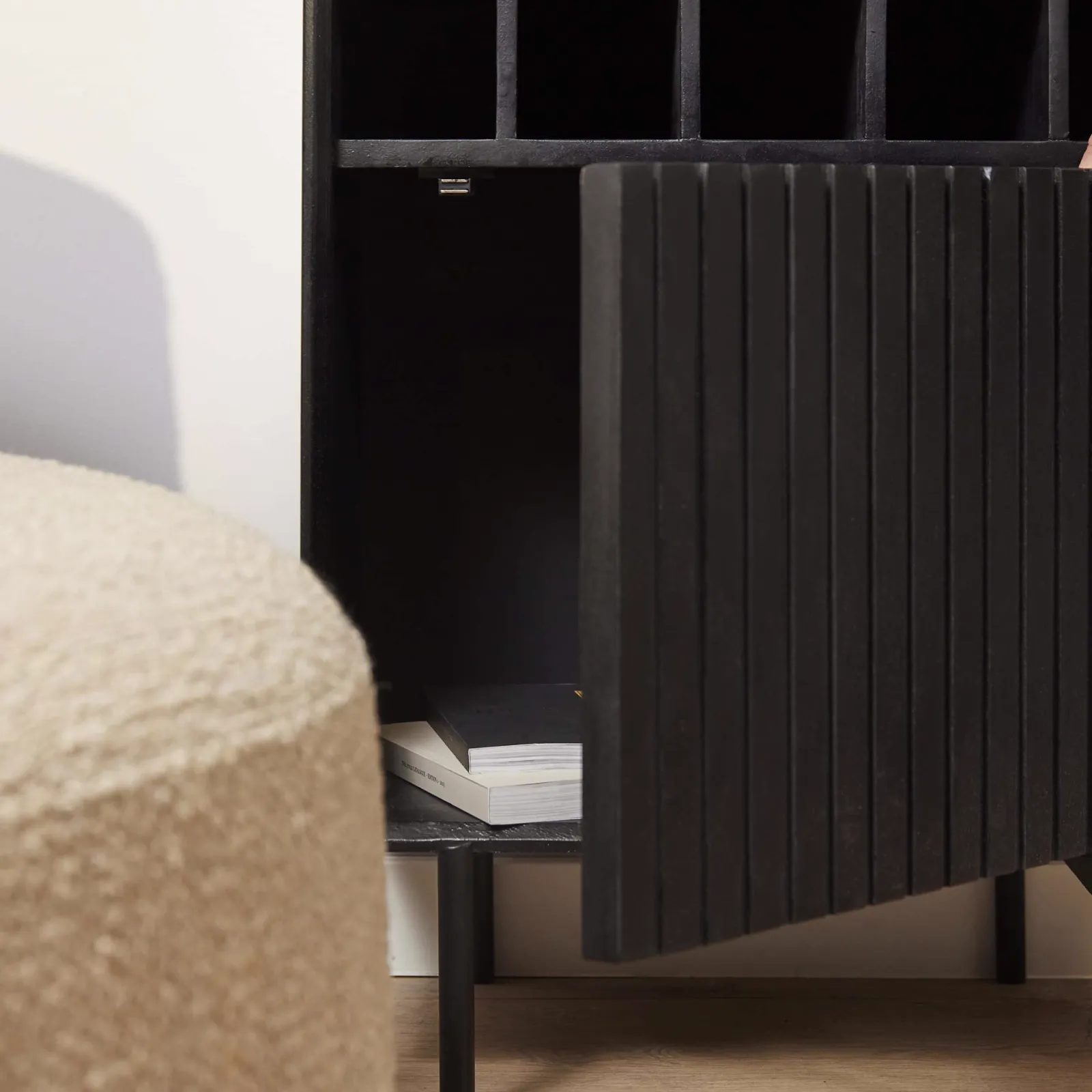 Detailopname van de Wijnkast Madison Black, met een geopende deur die boeken onthult en een beige poef op de voorgrond - Starfurn