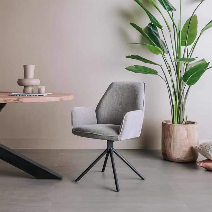 Der Amaro Sessel in Stoff Nature 452 Blue grey, drehbar, steht in einem modernen Wohnzimmer neben einem Holztisch und einer großen Pflanze - Tower Living
