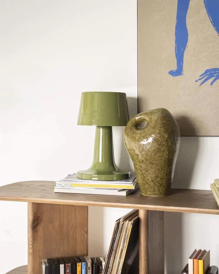 Tischleuchte Alvo Grün auf einem Holz-Sideboard mit Büchern und einer Vase, vor einer weißen Wand - By-Boo