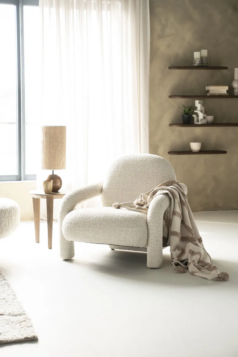 Sessel Monica - Taupe Asti in einem hellen Wohnzimmer mit einer Lampe und Regalen an der Wand - Eleonora