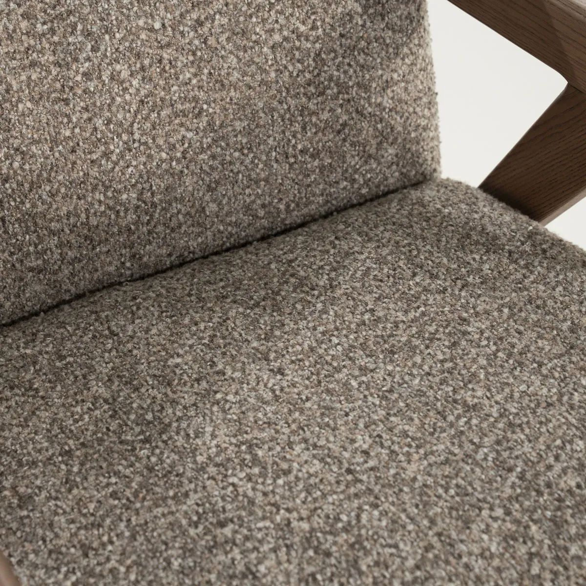 Detailansicht des Sessels Francis - taupe Flou, mit Fokus auf die Textur des taupefarbenen Bouclé-Stoffes und eine Holzarmlehne - Eleonora