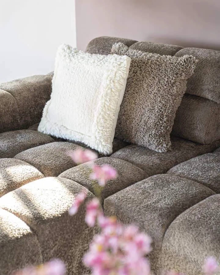 Zwei weiche Kissen, darunter Kissen Fez taupe, auf einem getufteten Sofa mit rosa Blumen im Vordergrund - By-Boo