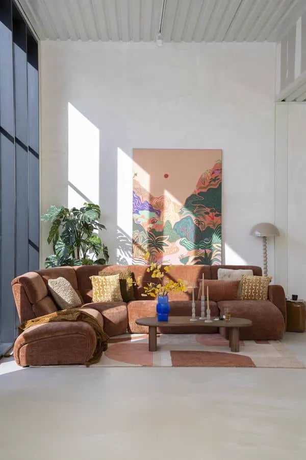 Ein beiges Kissen Mosa auf einem braunen Sofa, mit anderen Kissen und einem Couchtisch davor - By-Boo