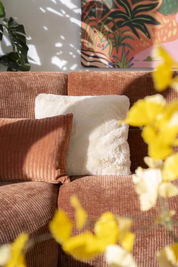 Zwei Kissen, darunter Kissen Mosa beige, auf einem braunen Sofa in einem hellen Wohnzimmer - By-Boo