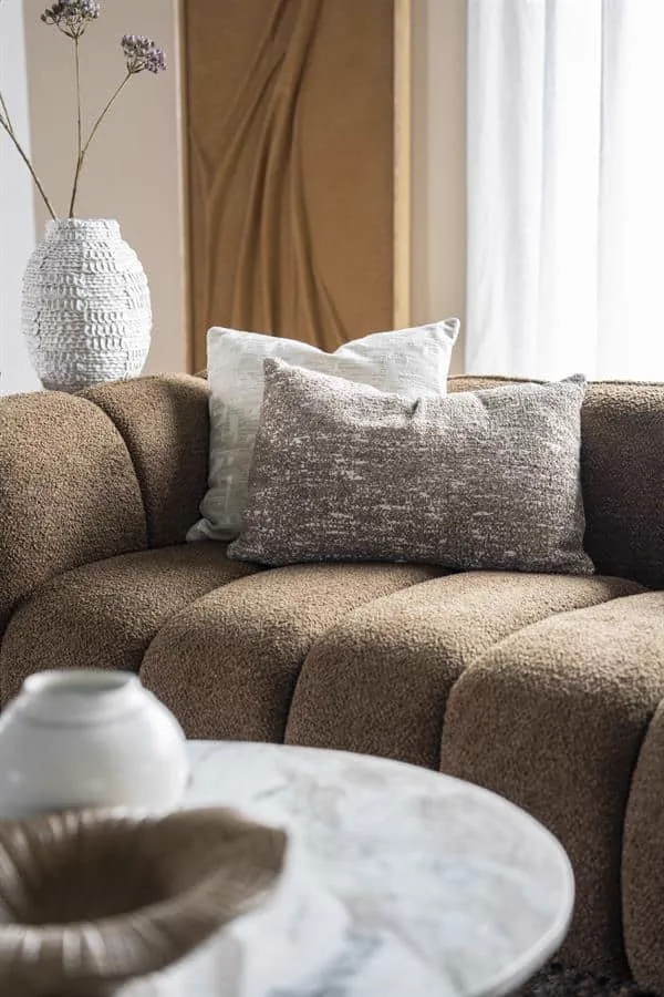 Das Kissen Bayo 40x60 cm - taupe liegt auf einem braunen Sofa in einem gemütlichen Wohnzimmer - By-Boo