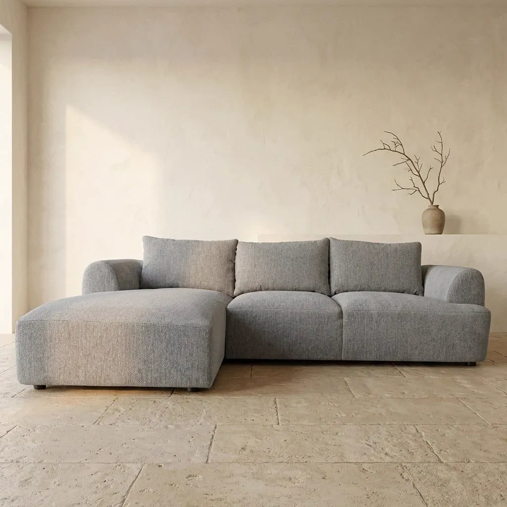 De Canterbury 2 5-AR + Chaise L - Mona 120 Taupe bank staat in een lichte studio met een vaas en takken op de achtergrond - Tower Living