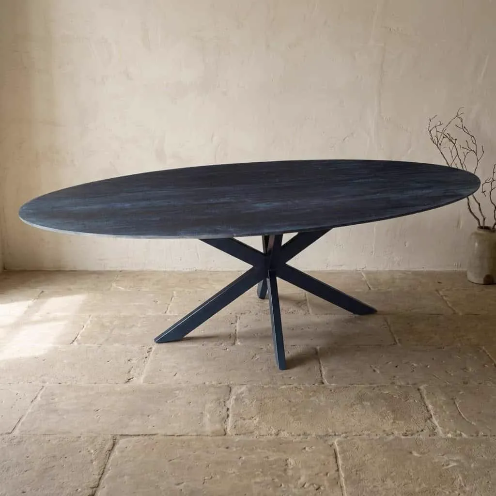 Der Esstisch Mangoholz oval schwarz Facettenkante steht mittig in einem Studio mit Steinboden - Mokana Furniture