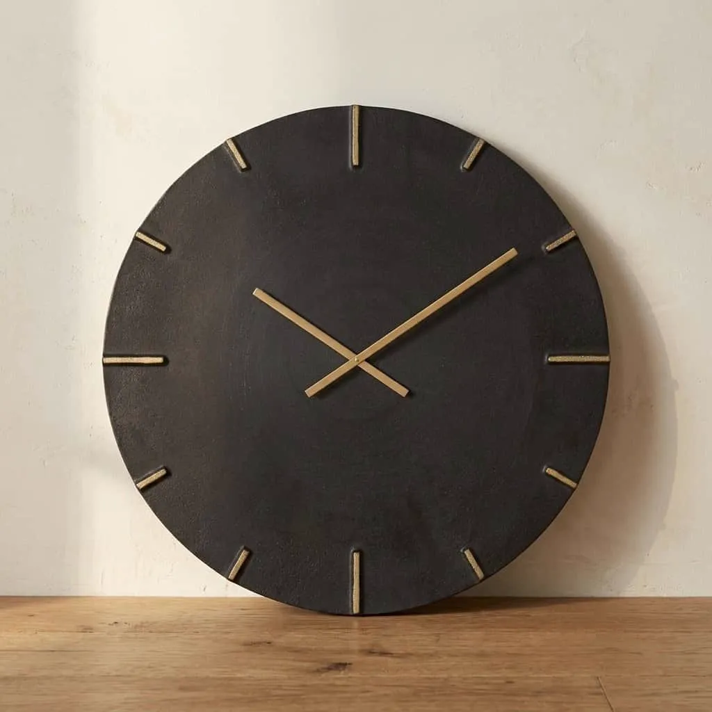 De Klok Bilal black/gold op een houten ondergrond, met een lichte muur op de achtergrond - Richmond Interiors