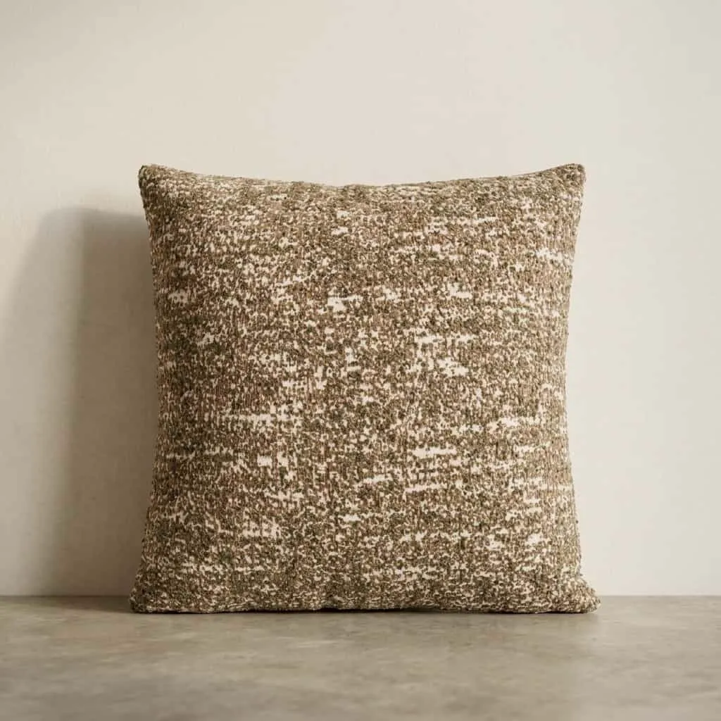 Ein taupefarbenes Kissen Bayo 45x45 cm mit melierter Textur, stehend vor einer hellen Wand - By-Boo