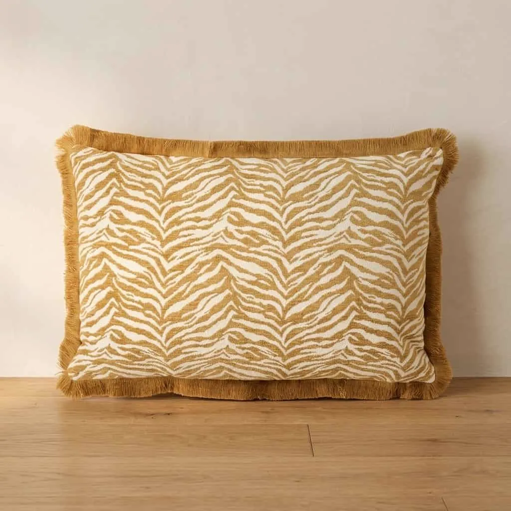 Kissen Tigra 40x60 cm - senf mit Fransen, stehend auf einem Holzboden vor einer weißen Wand - By-Boo