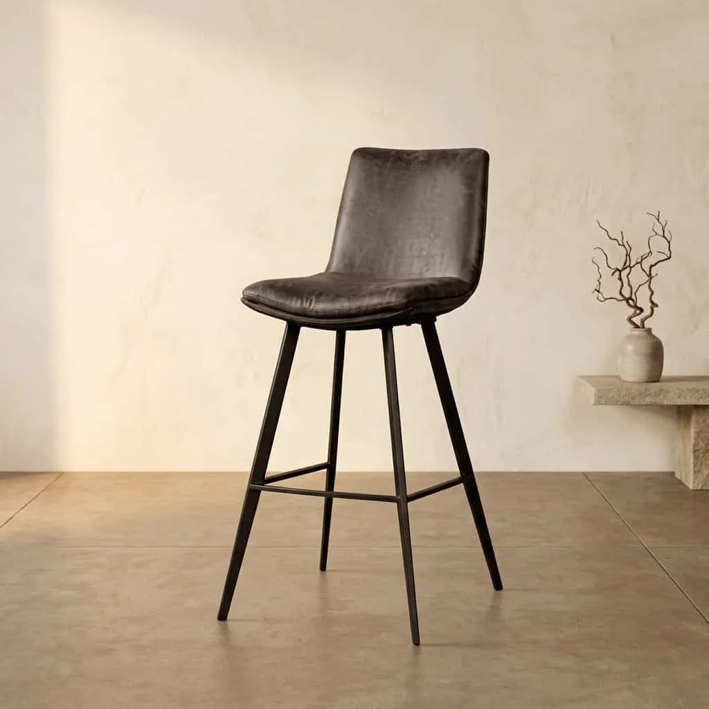 Pamplona Barstoel in antraciet stof, staand in een studio met een lichte wand en betonnen vloer - Tower Living